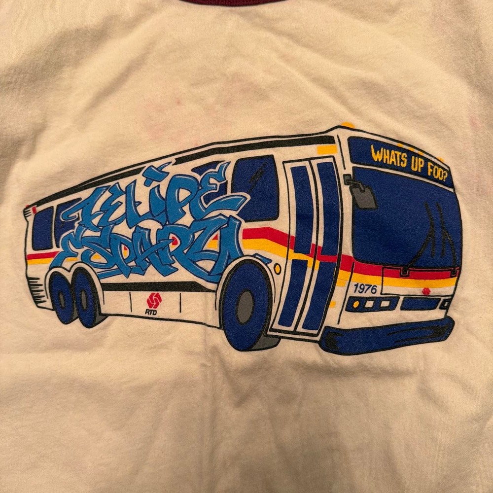 White graphic tee with blue bus featuring graffiti-style text and '1976'
